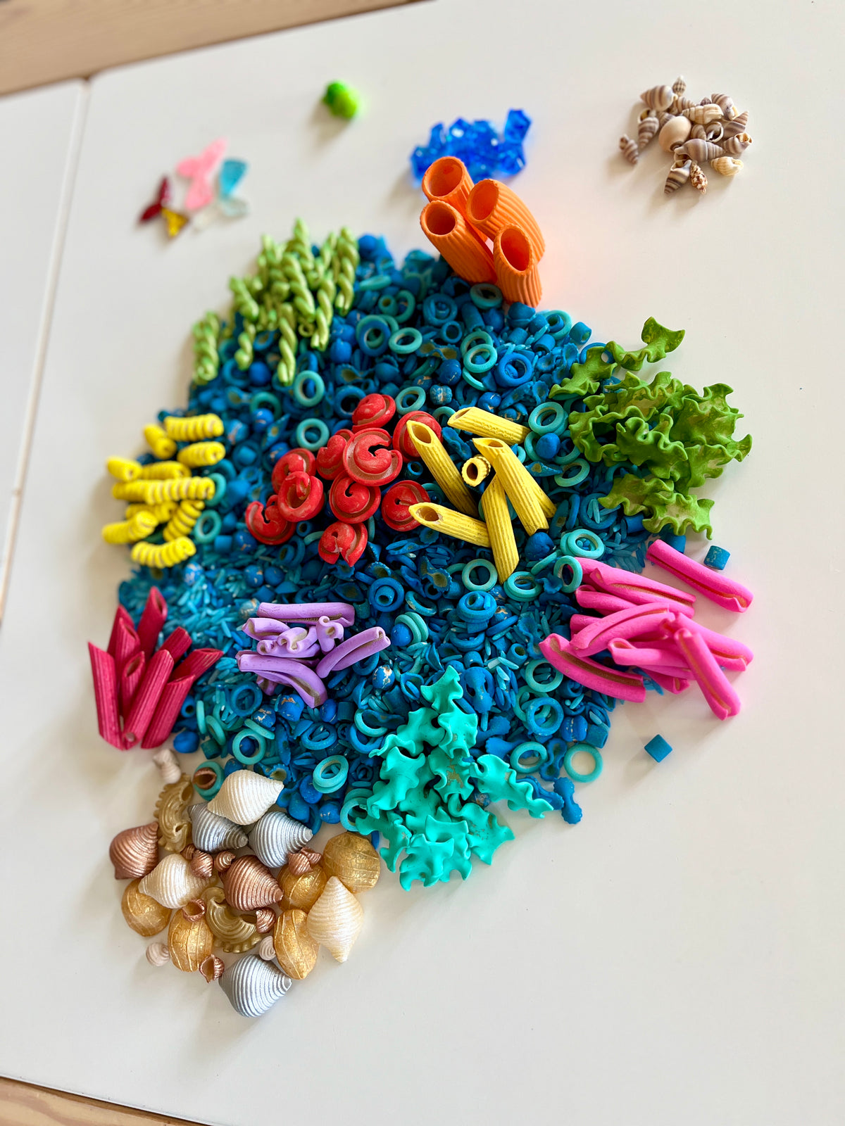 Colorful dried pasta shapes and seashells arranged on a white surface resembling an underwater coral scene.