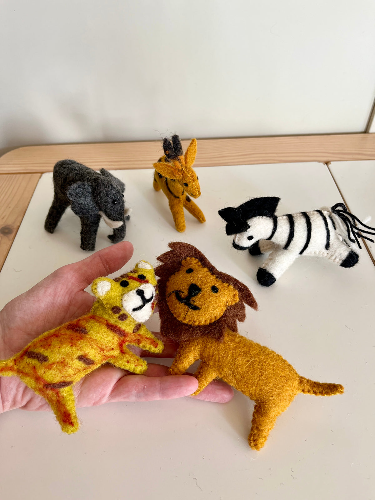 Five small felt animal figurines including a giraffe, elephant, lion, zebra, and cheetah on a light surface