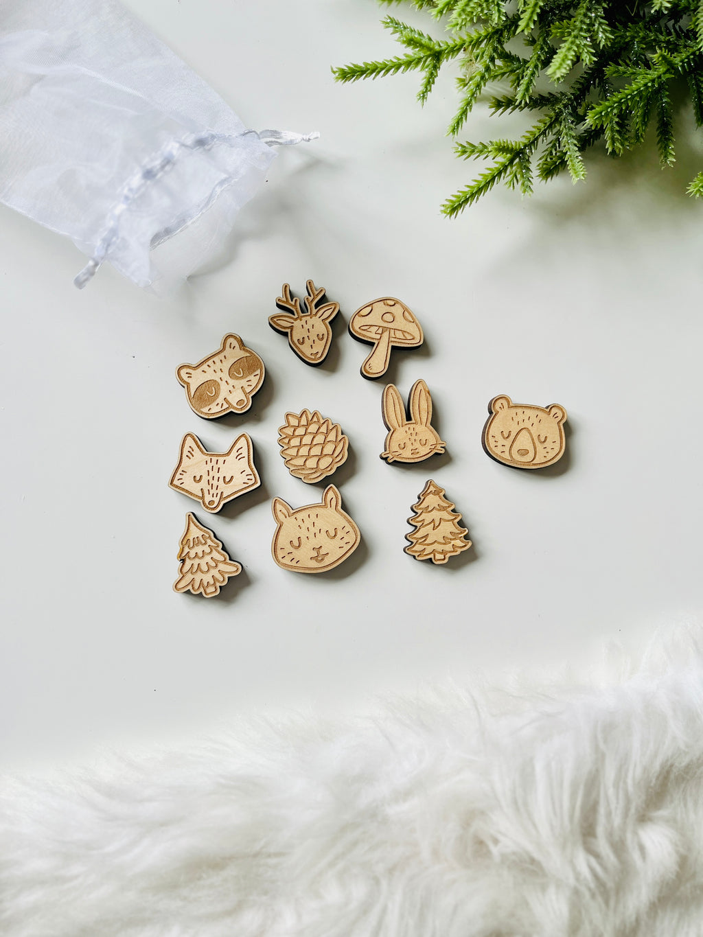 Small wooden cutouts featuring woodland animals, pinecones, mushrooms, and trees on white background with fabric pouch nearby
