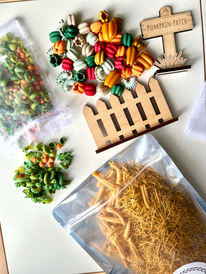 Colorful fall-themed dried pasta in clear bags with wooden fence and pumpkin patch sign on white surface