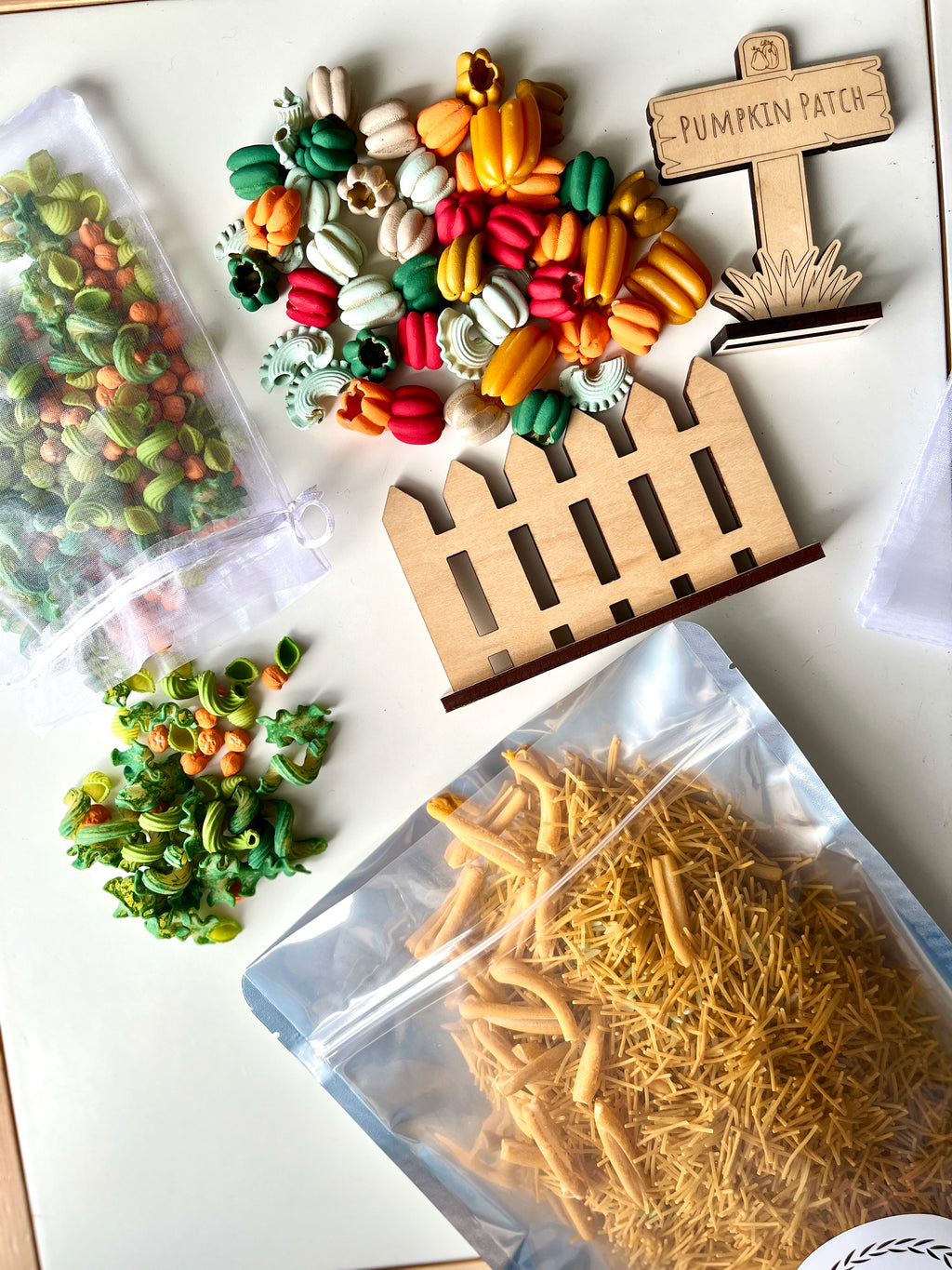Colorful fall-themed dried pasta in clear bags with wooden fence and pumpkin patch sign on white surface
