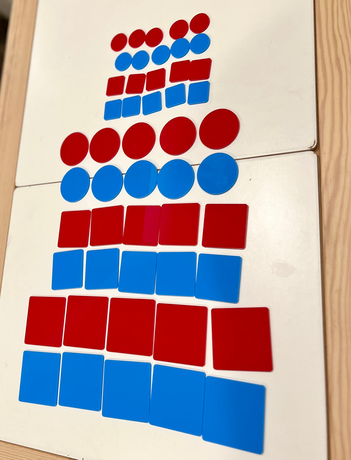 Red and blue circular and square plastic tokens arranged in rows on a white wooden surface
