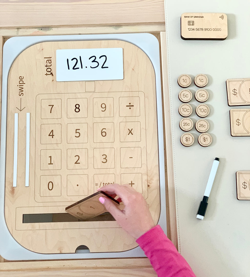 Wooden cash register insert with dry erase total, wooden credit card, coins, bills, and marker on white surface