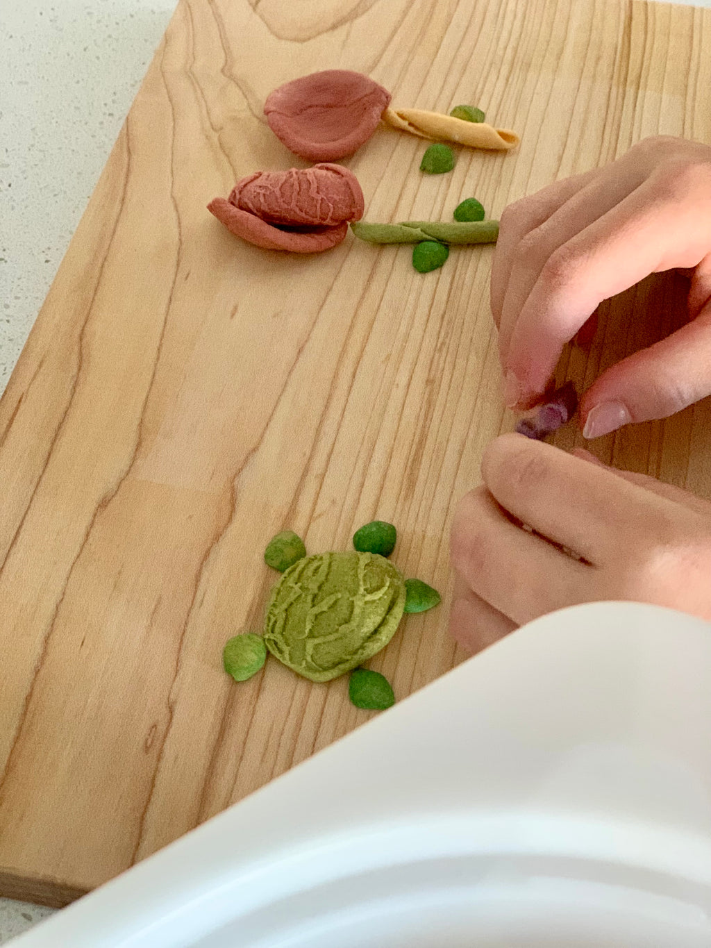 Hands shaping small colorful pieces resembling a turtle and flower on a light wooden surface
