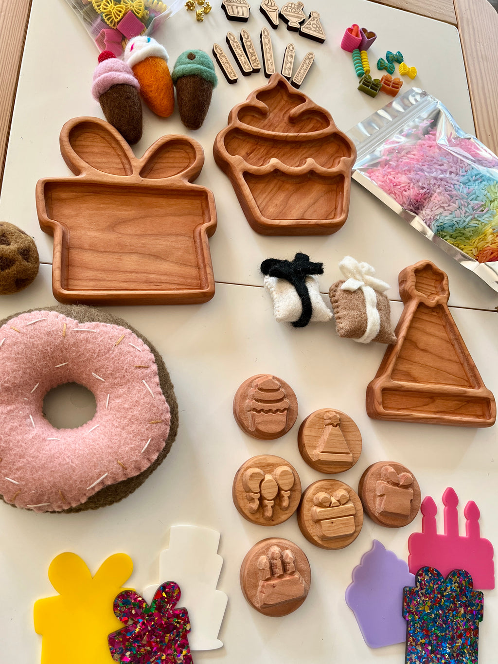 Wooden trays shaped like gift, cupcake, and party hat surrounded by felt treats, colorful sprinkles, and small wooden tokens