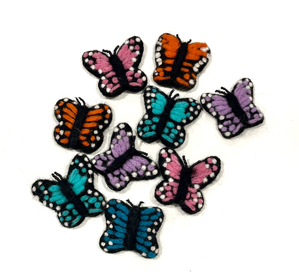 Collection of small felt butterfly shapes in pink, orange, blue, and purple with black and white spotted details on white background