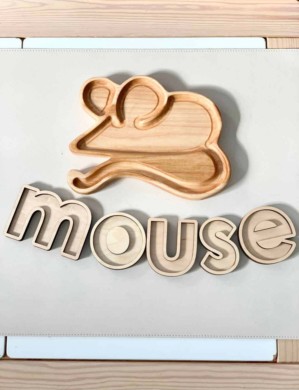Wooden mouse-shaped sensory tray with wooden letter inserts spelling mouse on white surface with wood edges
