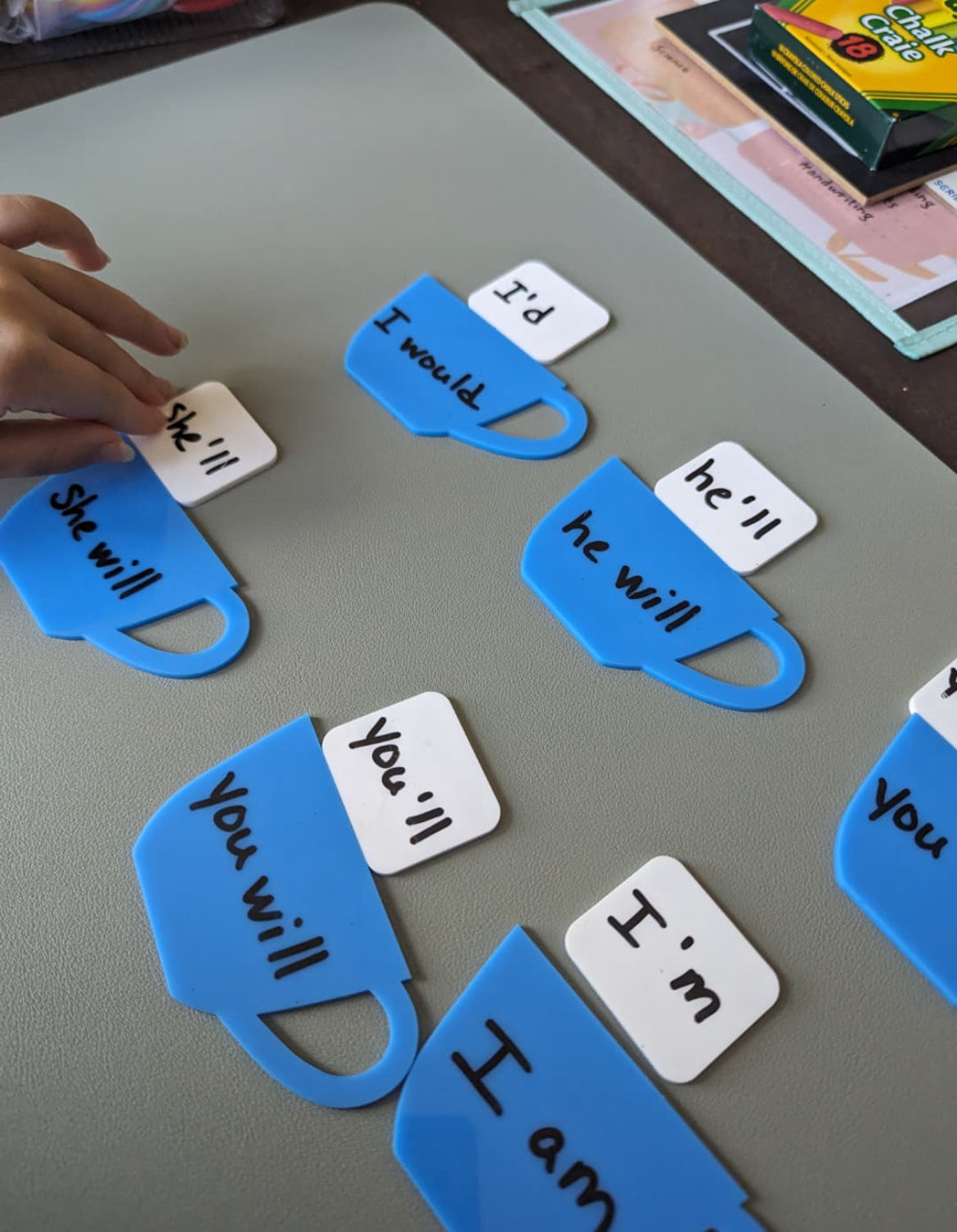 Blue plastic cup-shaped boards paired with white cards showing contractions and their full forms on a grey surface