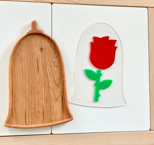 Wooden tray shaped like a bell with visible grain next to a clear acrylic bell-shaped piece featuring a red rose with green stem and leaves