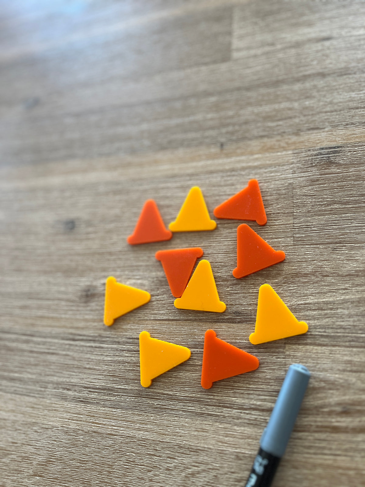 Twelve small orange and yellow cone shapes arranged on a wooden surface alongside a gray marker, Little Dry Erasables - Construction Cones, handcrafted, homeschool, education resources.
