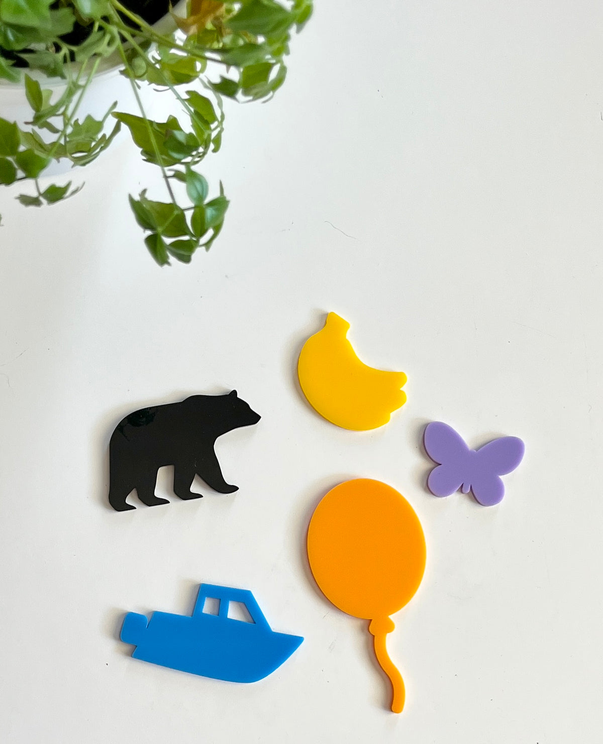 Five colorful acrylic shapes including a black bear, yellow chicken, purple butterfly, blue boat, and orange balloon on white surface