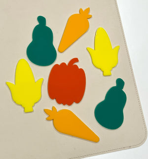 Colorful flat shapes of pumpkin, pear, carrot, and corn in green, orange, yellow, and red on a beige surface