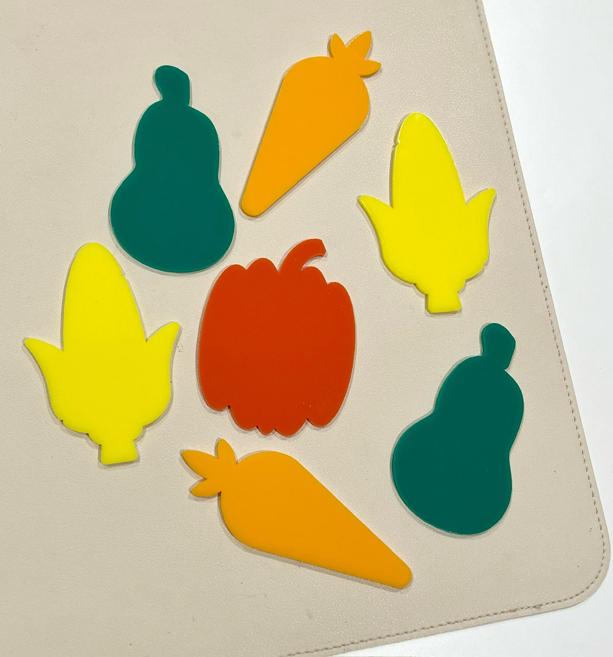 Colorful flat shapes of pumpkin, pear, carrot, and corn in green, orange, yellow, and red on a beige surface