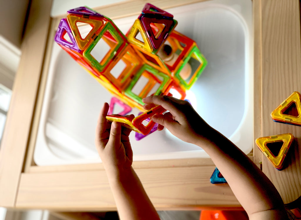 Child's hands assembling colorful magnetic tiles on frosted acrylic Flisat light table insert with wooden frame