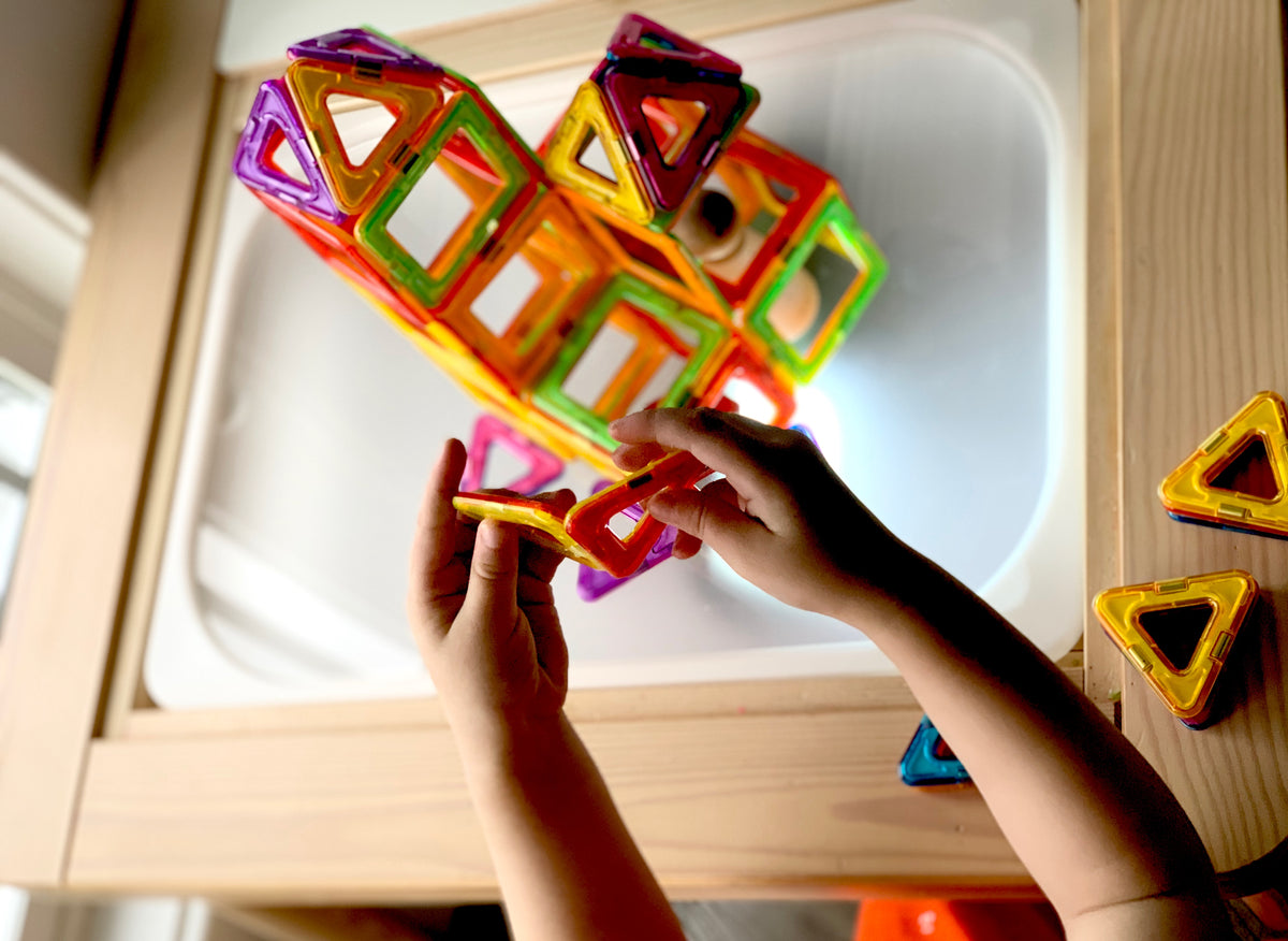 Child's hands assembling colorful magnetic tiles on frosted acrylic Flisat light table insert with wooden frame