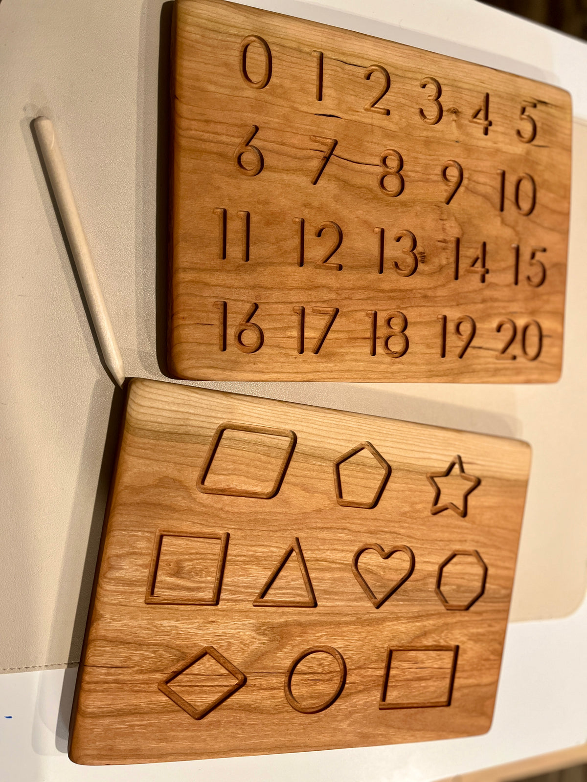 Wooden puzzle boards with engraved numbers and geometric shapes alongside a wooden stylus on a white surface