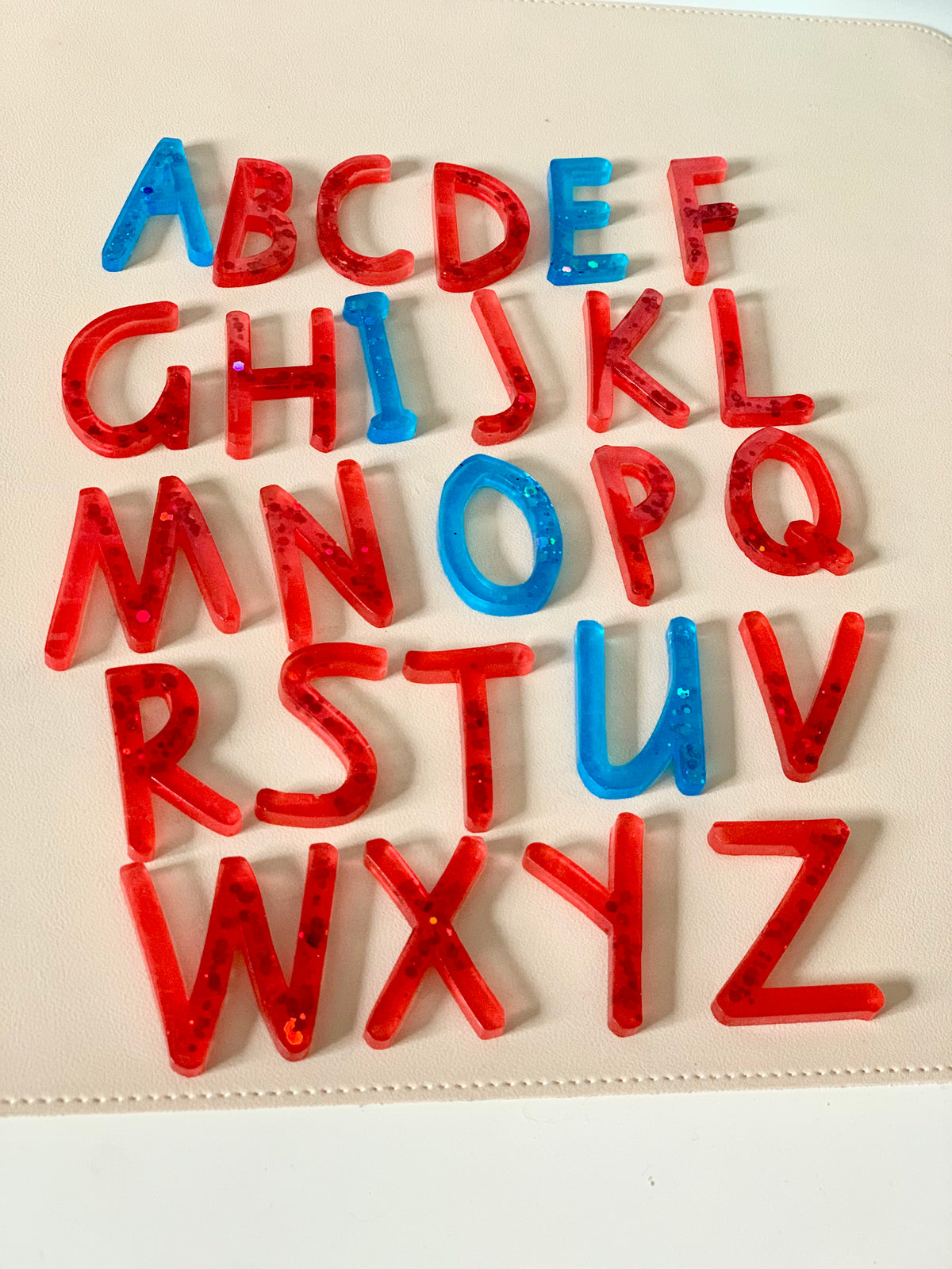 Translucent red and blue resin alphabet letters arranged loosely on a smooth light beige surface