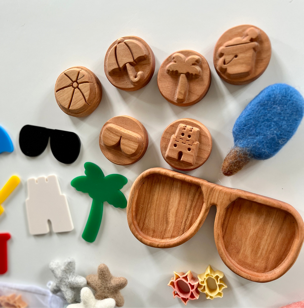 Wooden round tokens with summer icons including umbrella, palm tree, camera, and sunglasses-shaped tray on white surface