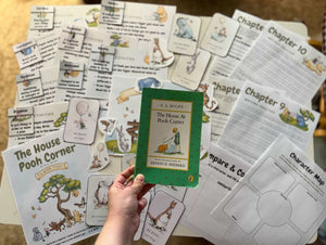 Hand holding a classic edition of The House at Pooh Corner surrounded by illustrated character cards, chapter worksheets, and activity pages for Digital Download or Print & Bound - The House at Pooh Corner Book Study, handcrafted, homeschool, education resources.