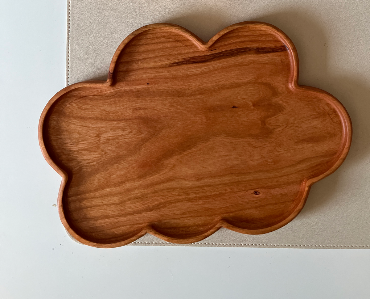 Smooth wooden tray shaped like a cloud with natural wood grain resting on a light surface
