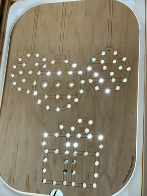 Wooden Flisat insert with light-up holes forming Christmas balls and gift shapes on light wood surface