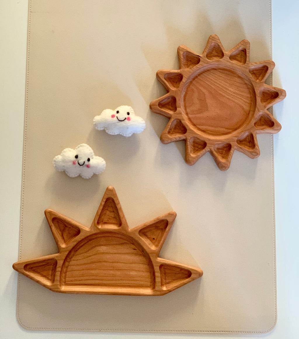 Two wooden sun-shaped trays on beige surface alongside two small smiling felt cloud decorations