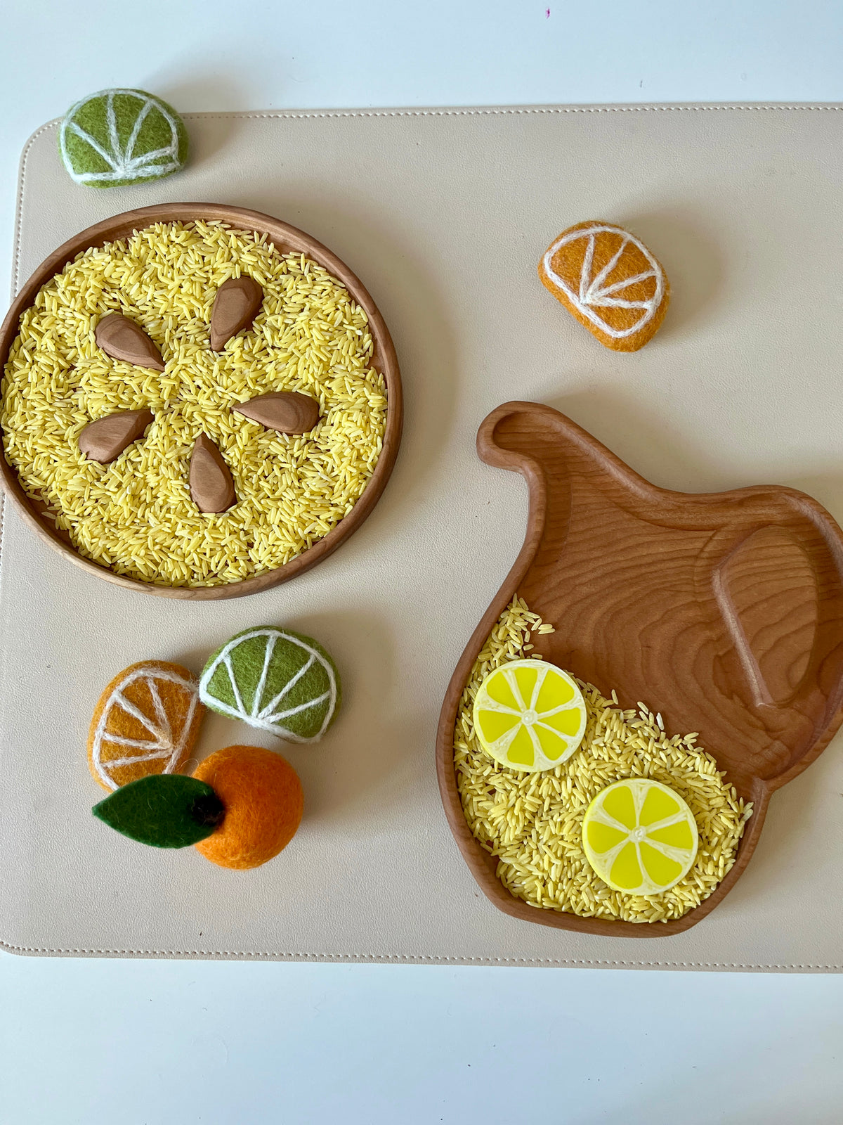 Wooden plates with yellow rice, felt citrus slices, a felt orange with leaf, and felt fruit wedges on a beige mat