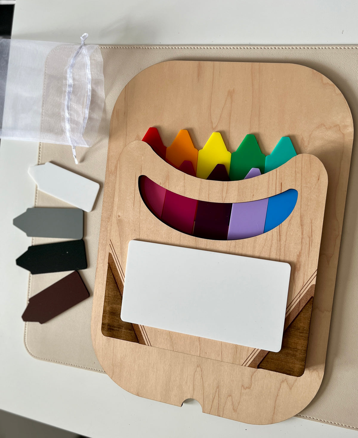 Wooden holder with rainbow-colored plastic plant markers and blank colored labels next to a white mesh bag on a light surface