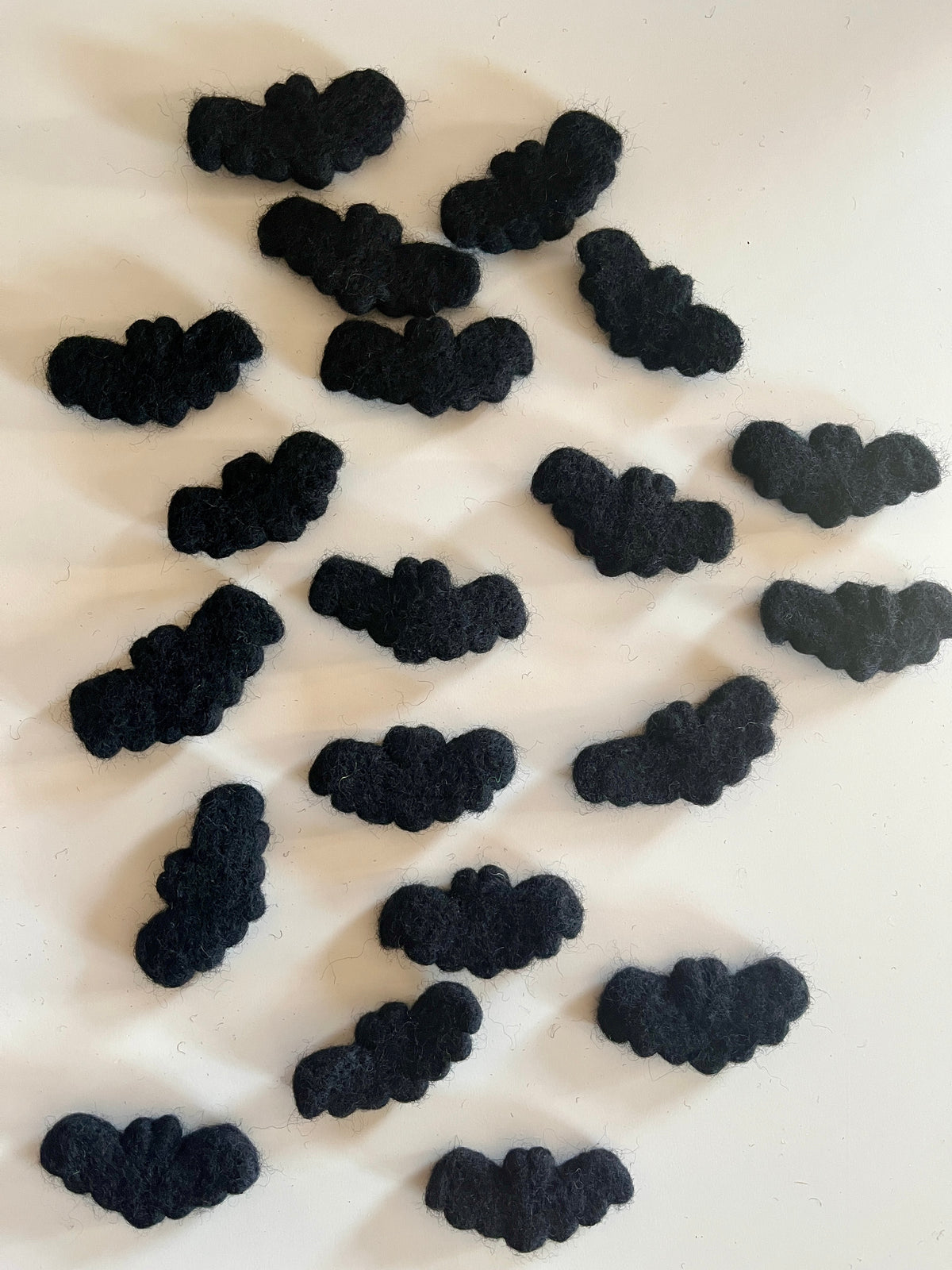 Scattered small black felt bat shapes arranged randomly on a white surface with soft shadows