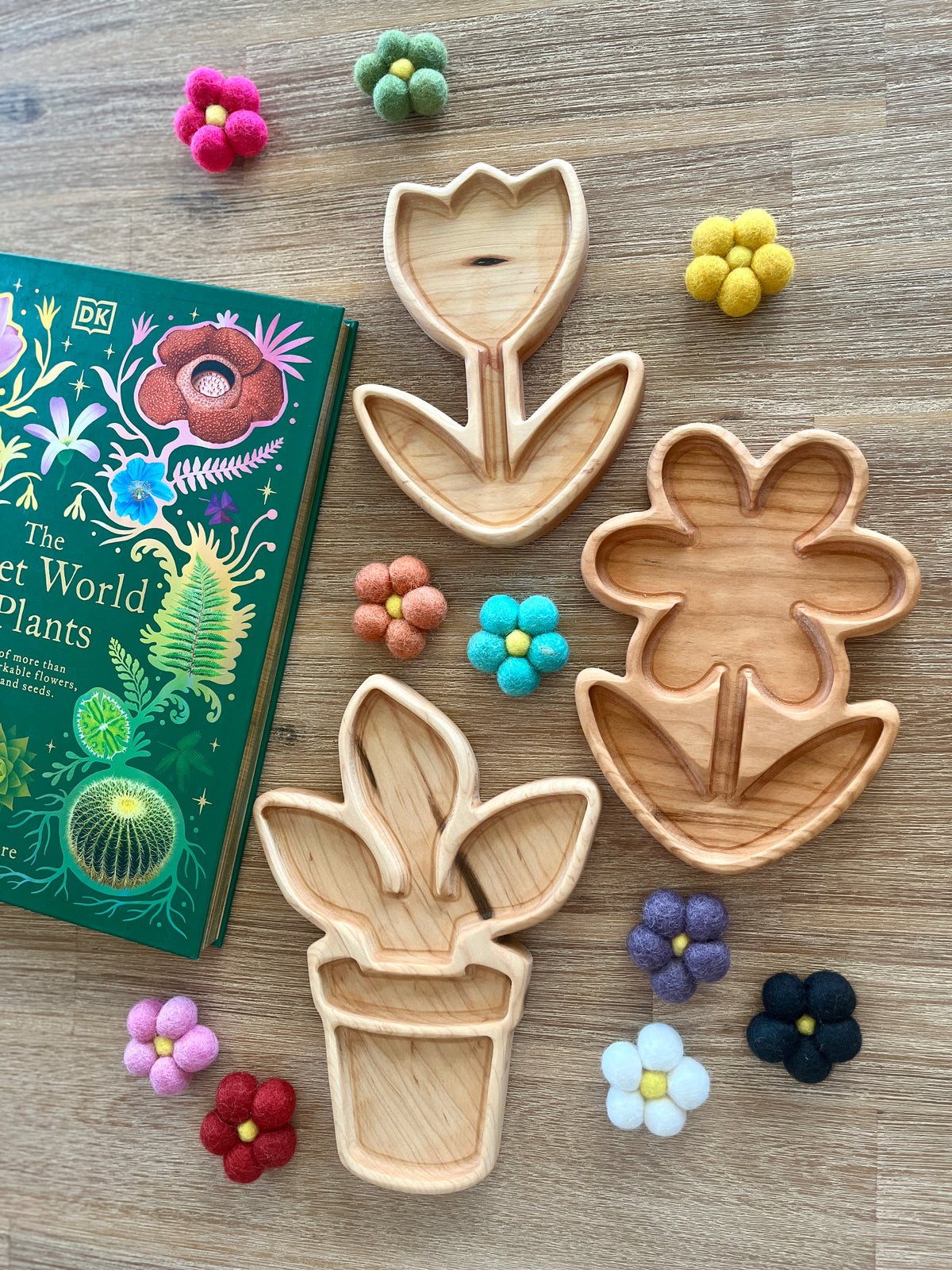 Plant and Flower Trays featuring three wooden floral-shaped compartments surrounded by colorful felt flower pom-poms and a plant-themed book, handcrafted homeschool education resources.