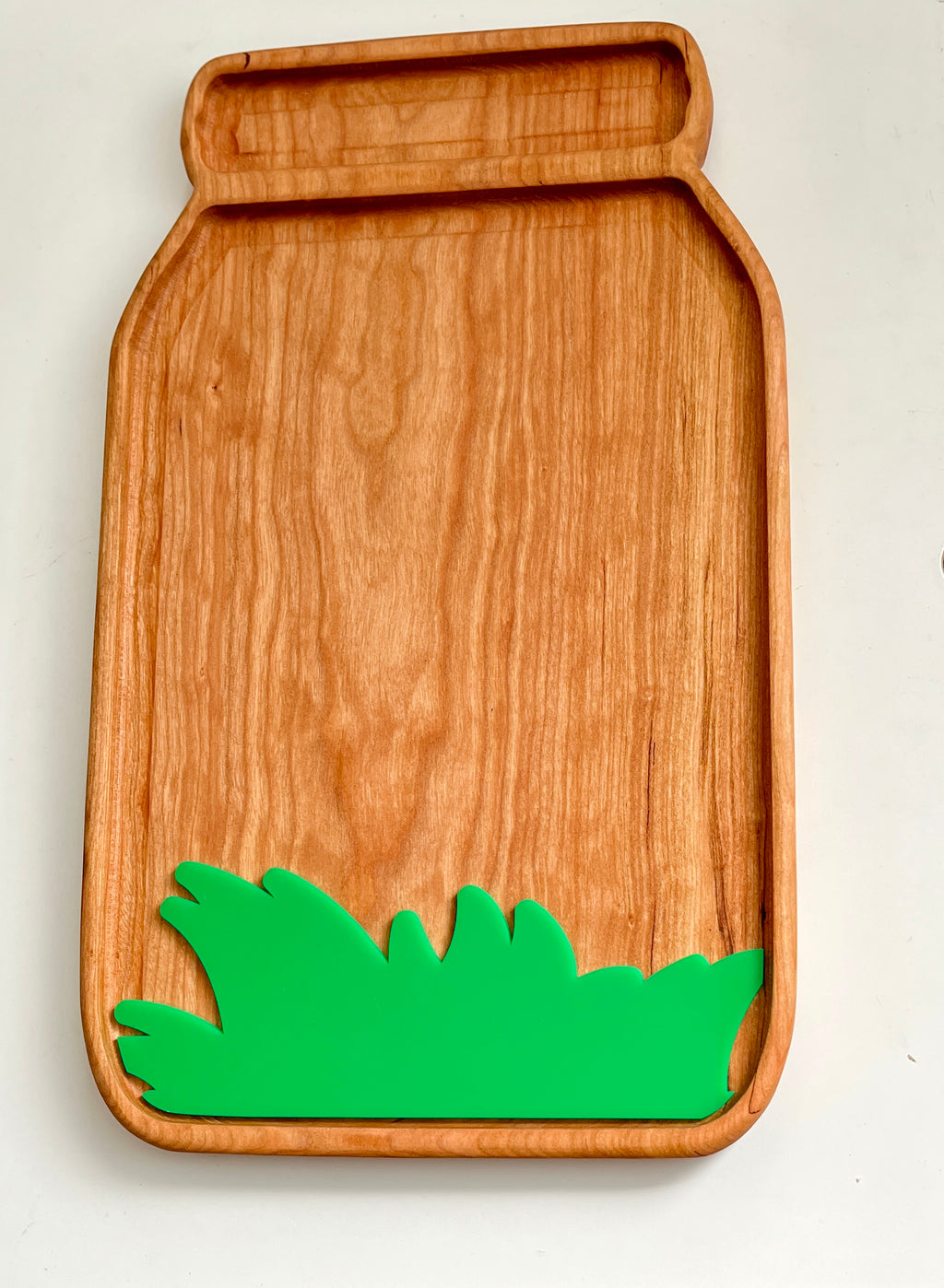 Wooden tray shaped like a jar with a smooth finish and a green grass-shaped decorative accent at the bottom edge