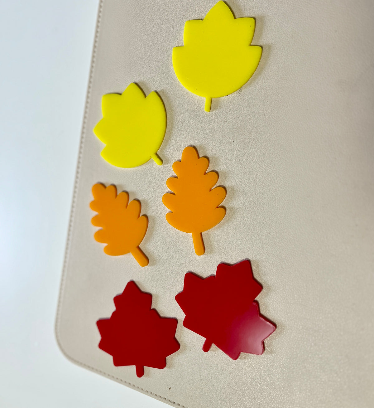 Three yellow, two orange, and two red leaf-shaped plastic pieces arranged on a beige surface