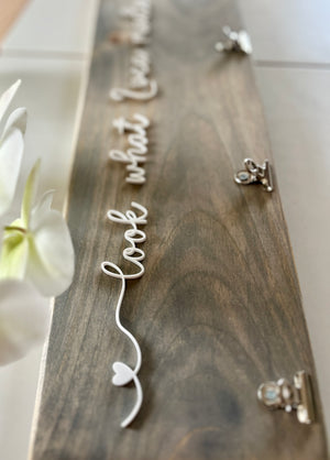 Natural wooden children’s artwork display sign with white cursive lettering and silver clips on light wood grain background