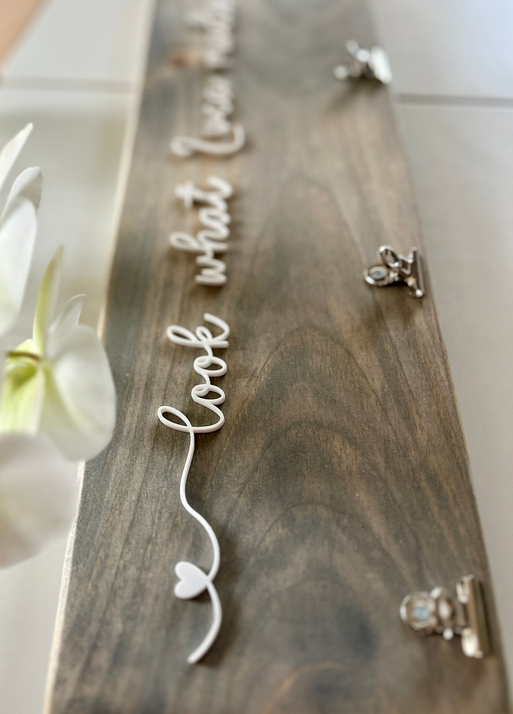 Natural wooden children’s artwork display sign with white cursive lettering and silver clips on light wood grain background