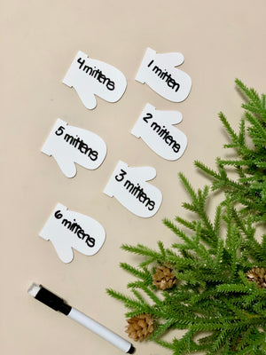 Set of six white dry erasable mitten-shaped flashcards numbered one to six with black dry erase marker and pine branch decor