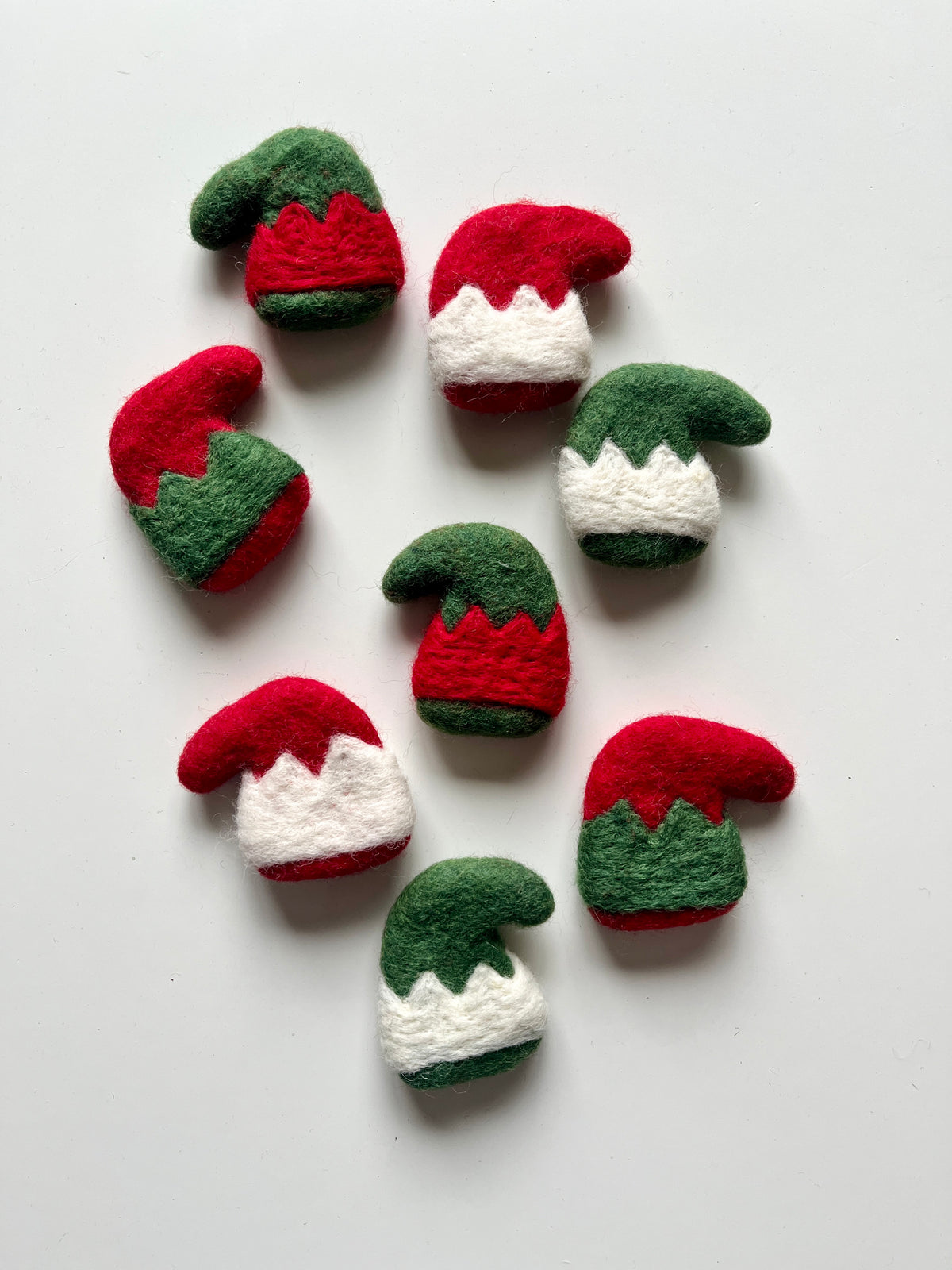 Felt Christmas elf hats in red, green, and white with zigzag trim arranged on a white background