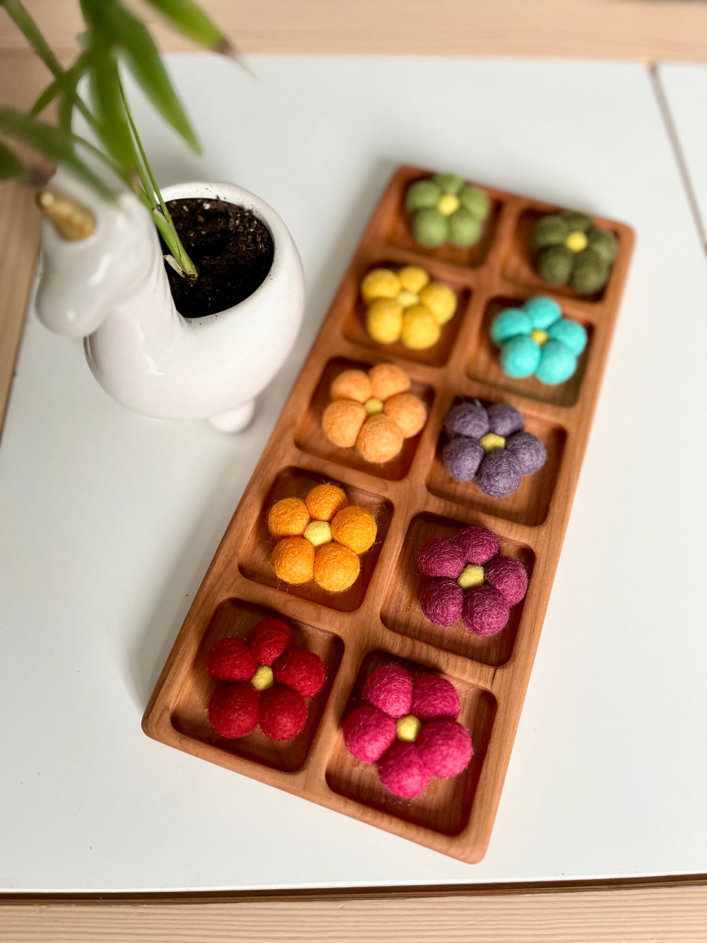 Wooden tray with nine compartments each holding a colorful felt flower in various bright shades on a white surface