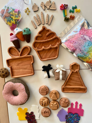 Wooden trays shaped like cupcake, gift box, and party hat with felt desserts, colorful beads, and rainbow-dyed rice on beige surface