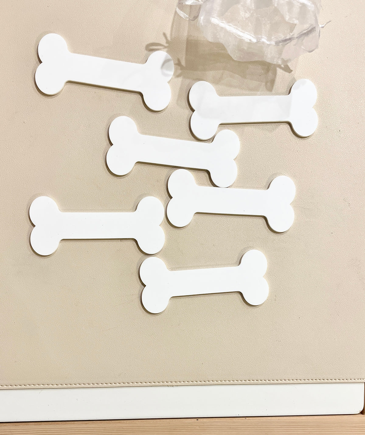 Six plain white bone-shaped tags arranged on a beige surface next to a clear plastic object