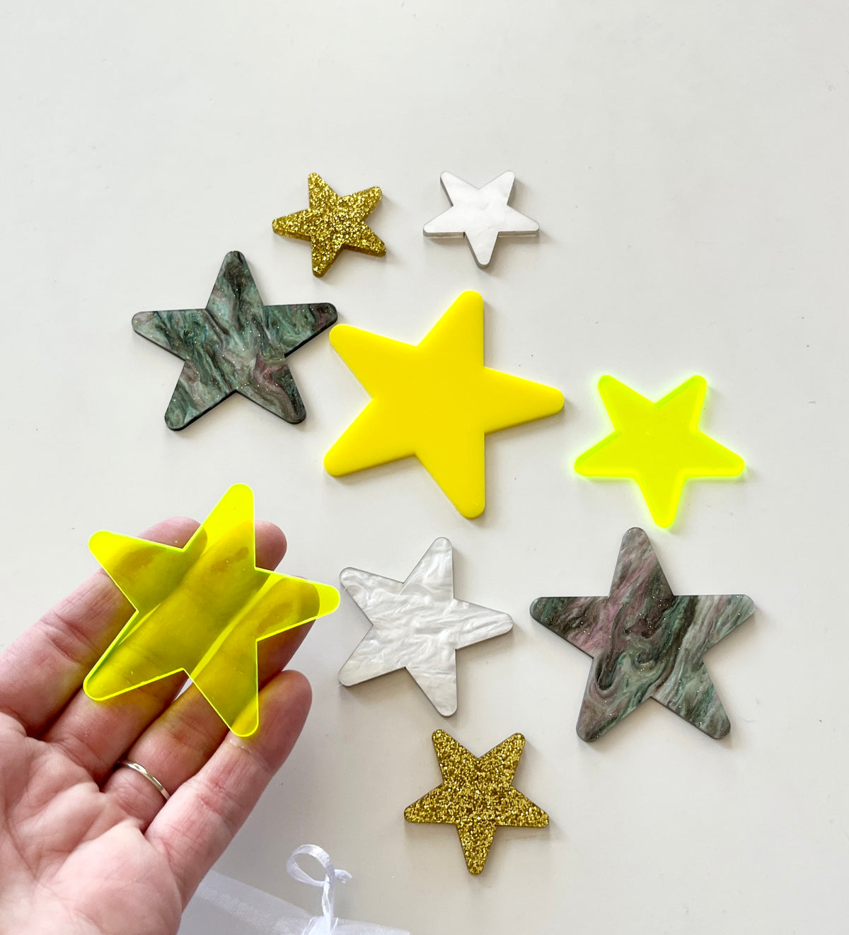 Various decorative star shapes in yellow, gold glitter, white marble, and green marble finishes on a white surface