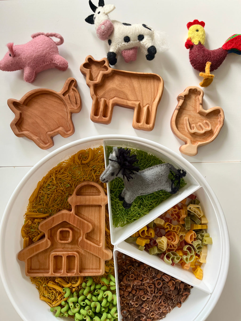 Wooden farm animal trays shaped like pig, cow, and chicken with felt farm animals and a divided tray of colorful pasta and noodles