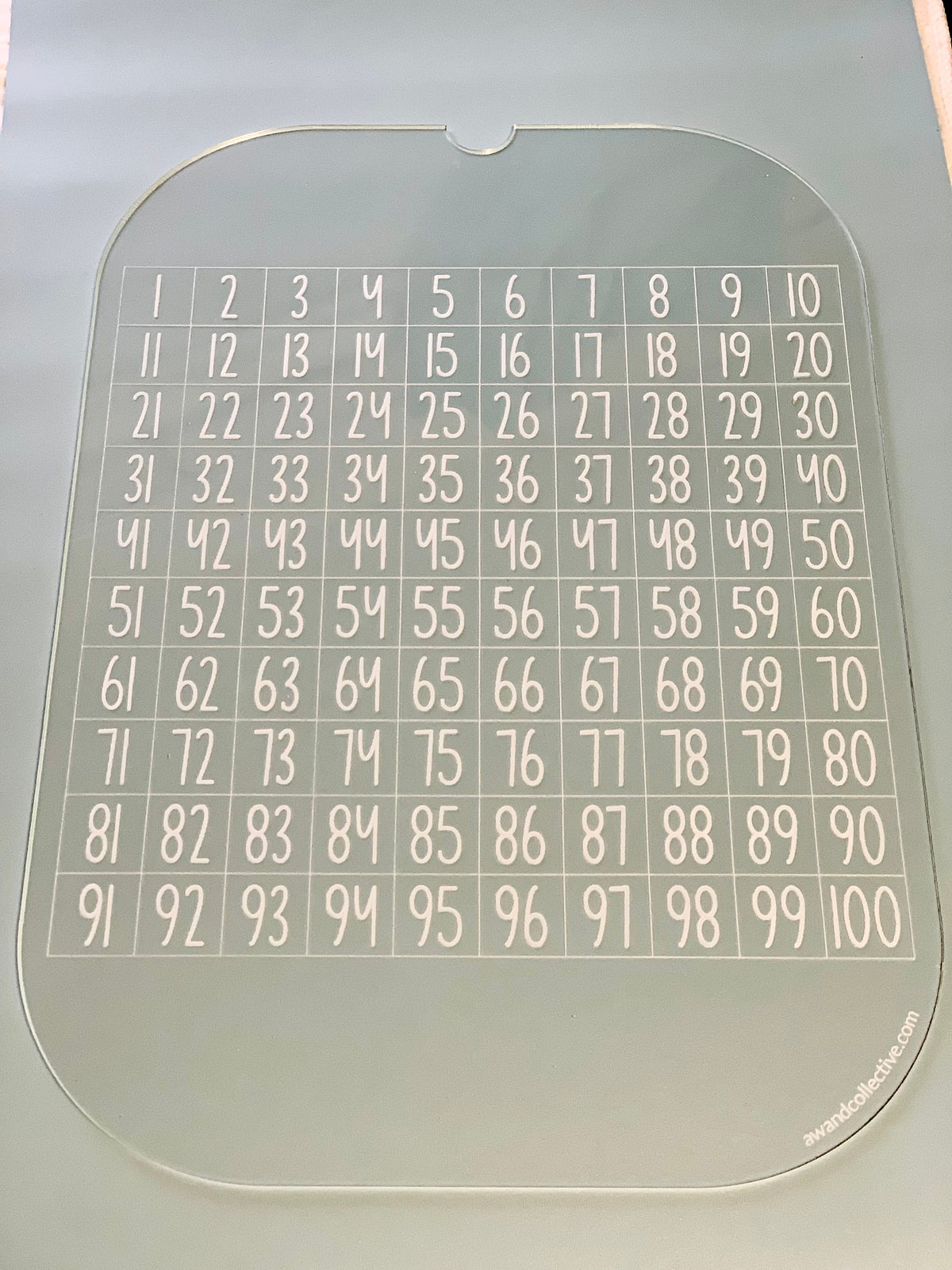 Transparent acrylic board with numbers 1 to 100 arranged in a 10 by 10 grid on a gray surface