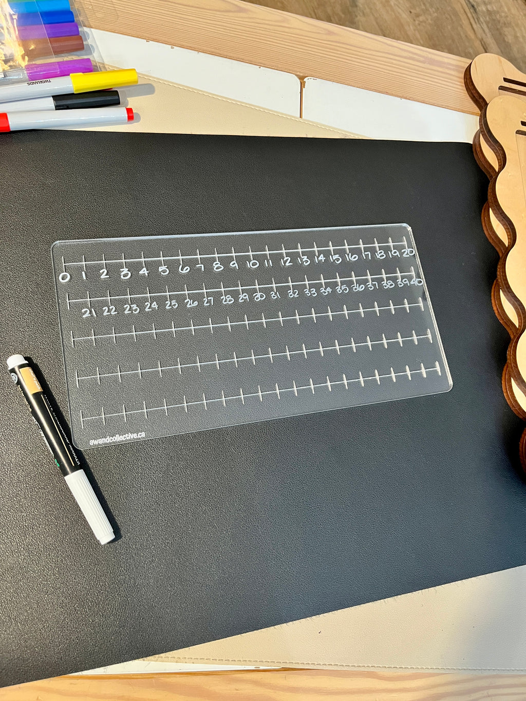 Transparent acrylic number line board with markings from 0 to 40, placed on black surface with white marker nearby