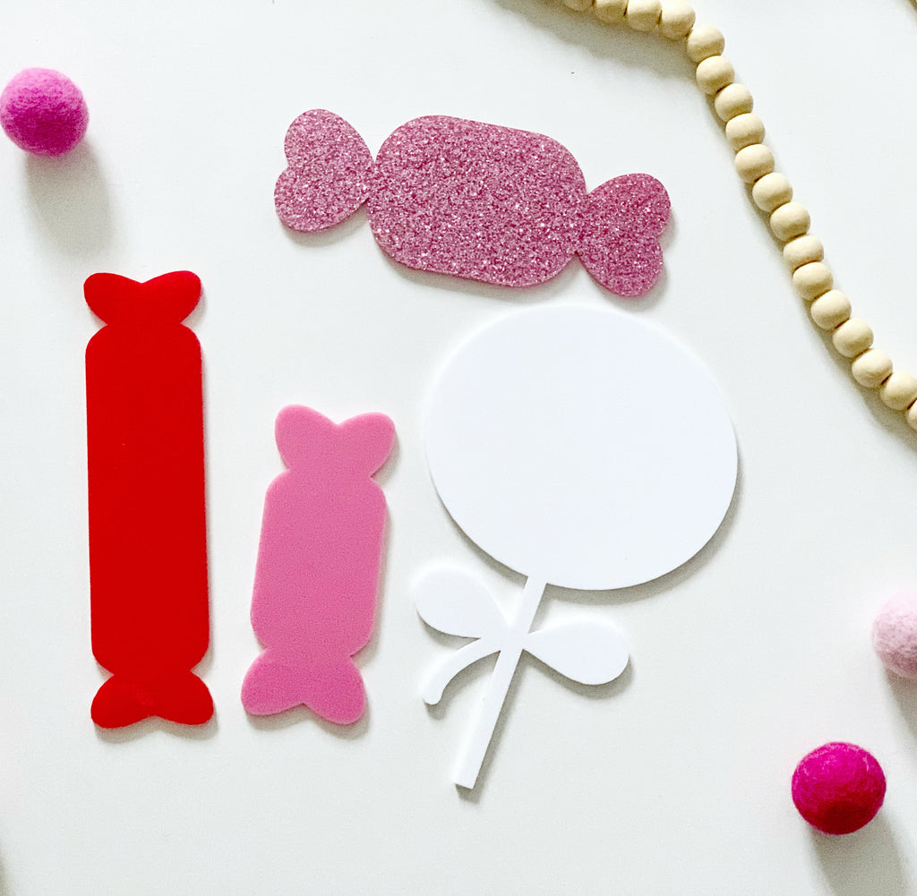 Four small dry erase candy-shaped boards in red, pink, glittery pink, and white with decorative beads on white surface