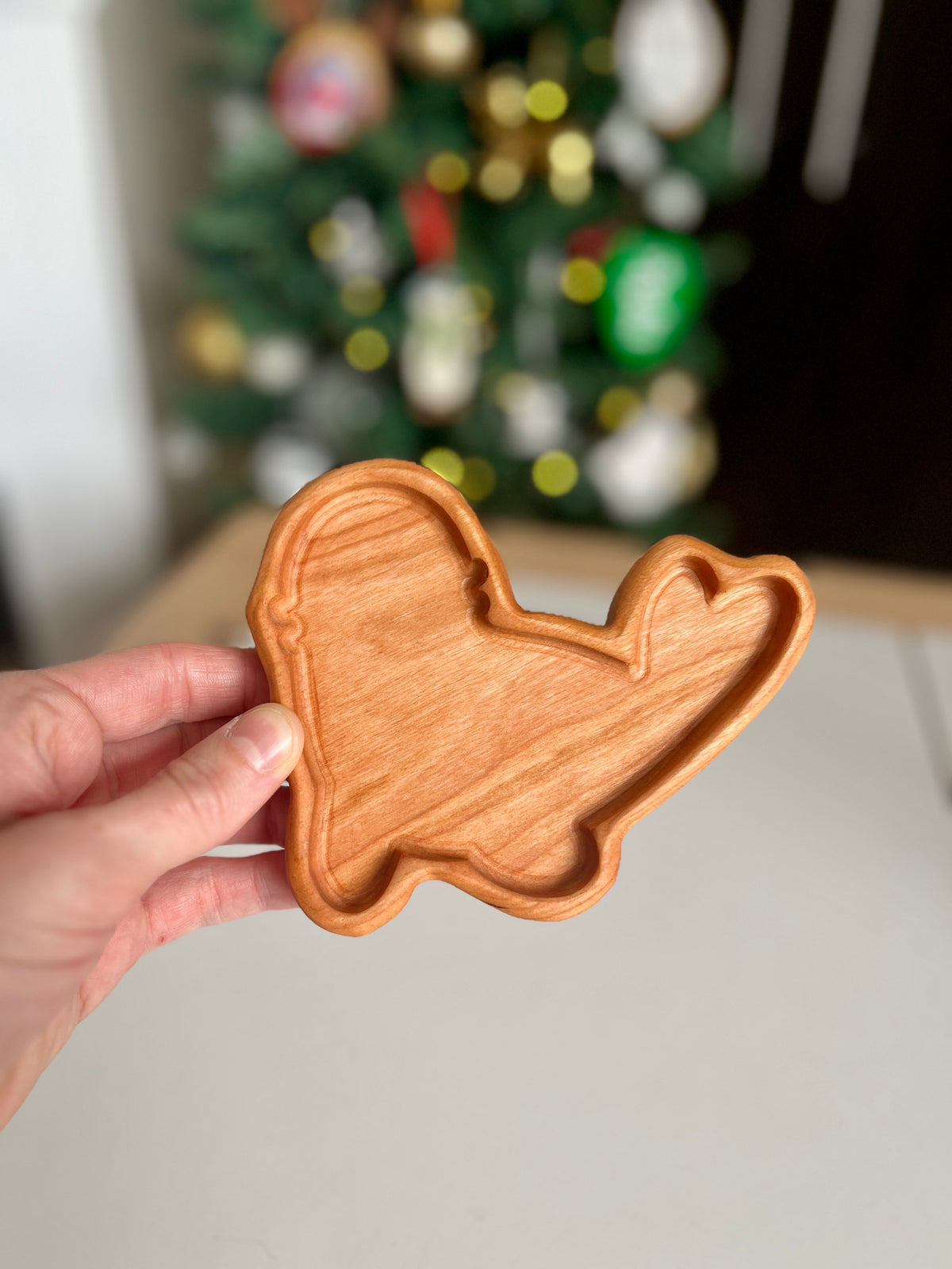 Hand holding a small wooden tray carved in the shape of a whale with a heart-shaped tail against a blurred background.