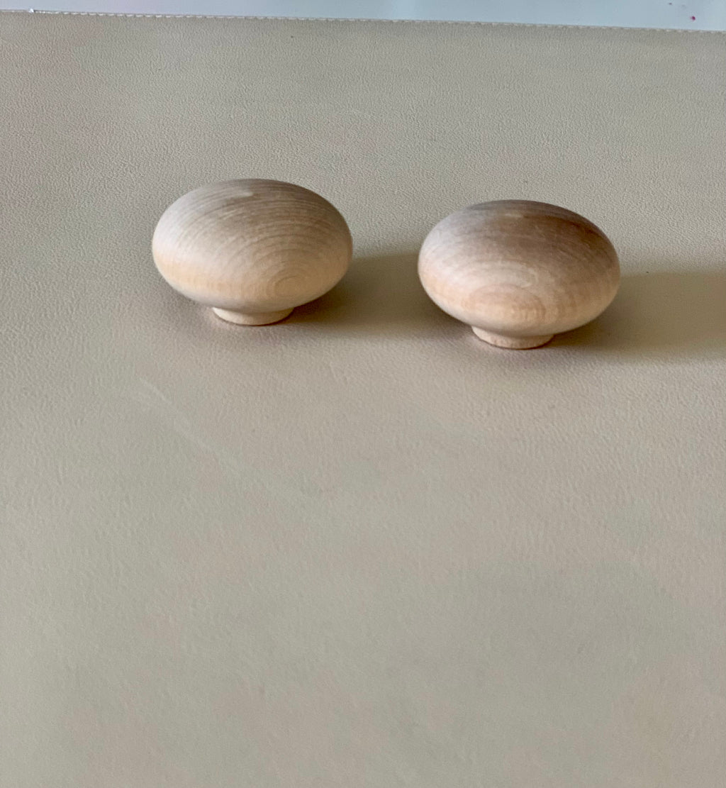 Two smooth rounded natural wood knobs placed on a beige surface with soft lighting