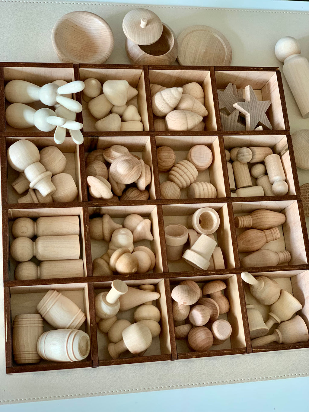 Collection of various unfinished natural wood shapes and small objects organized in a wooden compartment box