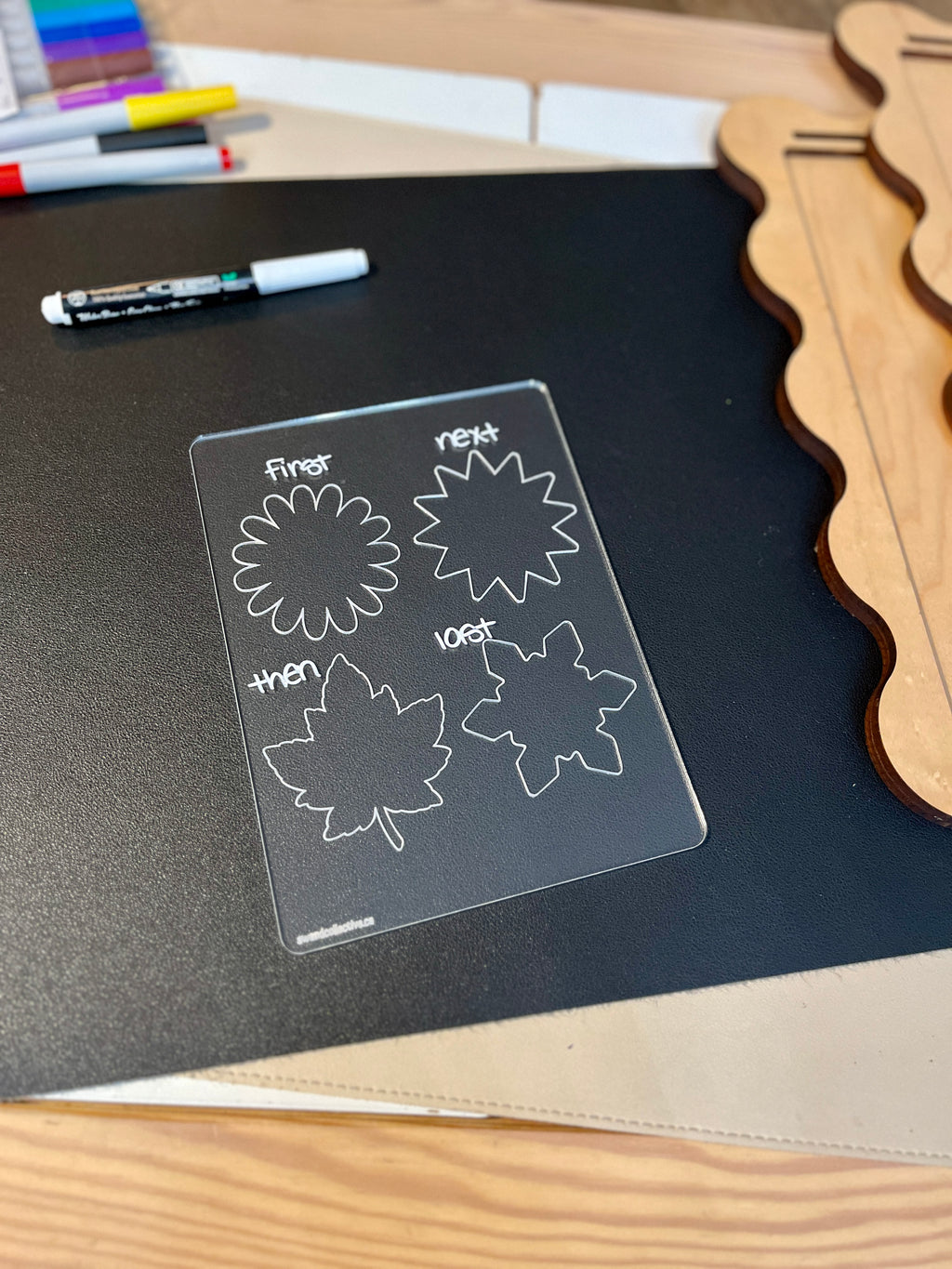 Clear plastic board with sequence words first, next, then, last paired with flower and leaf outlines on black surface