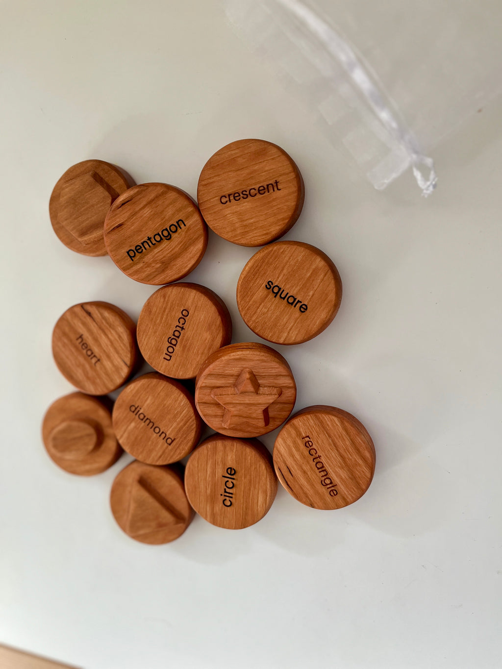 Set of round wooden discs engraved and labeled with various geometric shapes on a white surface next to a clear bag string