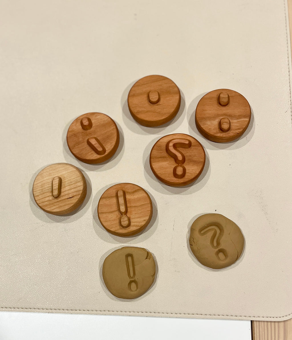 Seven round wooden tokens with raised punctuation symbols and two matching clay pieces with imprints on a light surface